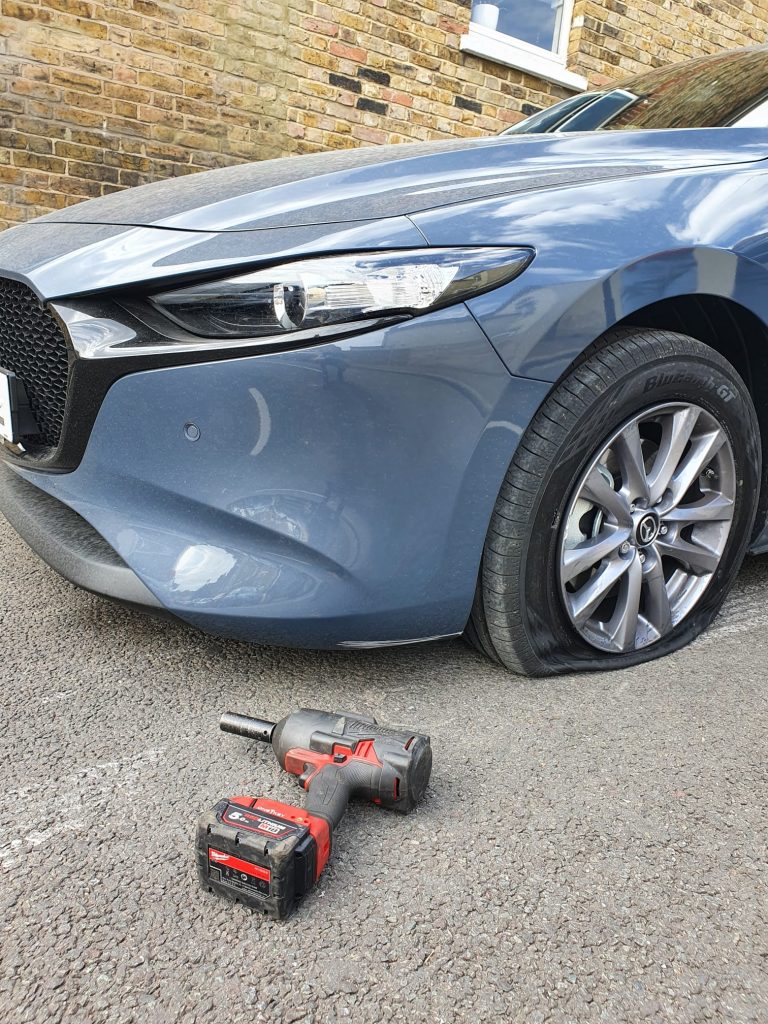 a car with a flat tire on the ground next to a drill